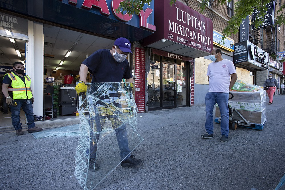 A worker removes a smashed plate glass window as a deliveryman brings in boxes of goods at Good Life Pharmacy, Monday, June 8, 2020, in New York. The pharmacy was broken into during protests a week ago. After three bleak months, New York City will try to turn a page when it begins reopening Monday after getting hit first by the coronavirus, then an outpouring of rage over racism and police brutality. (AP Photo/Mark Lennihan)