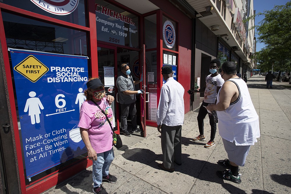 A store employee, second from left, talks to waiting customers at P.C. Richard and Son electronics and appliance store, Monday, June 8, 2020, in the Bronx borough of New York. The store is only providing pick-up orders on Monday. It will reopen its doors later in the week. After three bleak months, New York City will try to turn a page when it begins reopening Monday after getting hit first by the coronavirus, then an outpouring of rage over racism and police brutality. (AP Photo/Mark Lennihan)