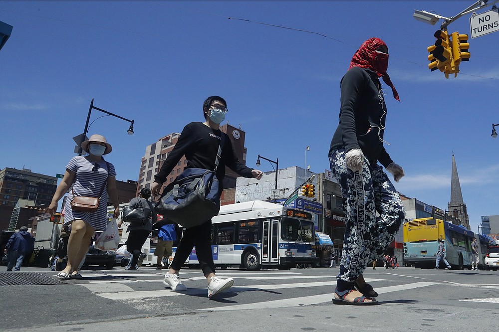Pedestrians wear face coverings and protective masks as they cross Mains street, Monday, June 8, 2020, in the Flushing section of the Queens borough of New York. After three bleak months, New York City will try to turn a page when it begins reopening Monday after getting hit first by the coronavirus, then an outpouring of rage over racism and police brutality. (AP Photo/Frank Franklin II)