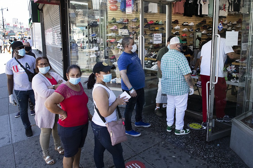 People with their face masks stand in line to enter a Sneaker Box after it reopens, Monday, June 8, 2020, in the Bronx borough of New York. After three bleak months, New York City will try to turn a page when it begins reopening Monday after getting hit first by the coronavirus, then an outpouring of rage over racism and police brutality. (AP Photo/Mark Lennihan)