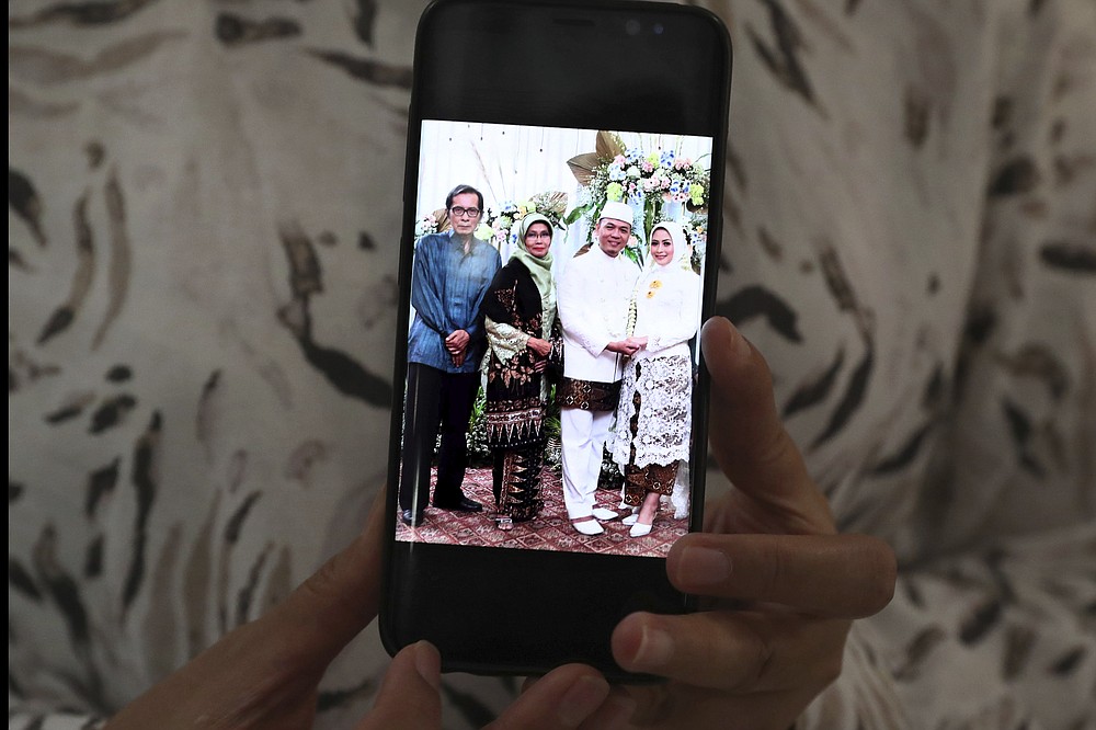 Eva Rahmi shows her mobile phone that displays her parents Teten Syamsir, left, and Ismy Latifah, second from left, and her husband Andi Saloko, second from right, on their wedding day, in Jakarta, Indonesia, Tuesday, June 2, 2020. Salama worries that authorities in Jakarta, Indonesia’s sprawling capital, are acting too soon to lift restrictions put in place two months ago to fight the spread of the coronavirus. This has raised concerns among some, with experts warning that reopening too soon can cause Jakarta to be hit with a second wave of the virus. (AP Phtoto/Tatan Syuflana)