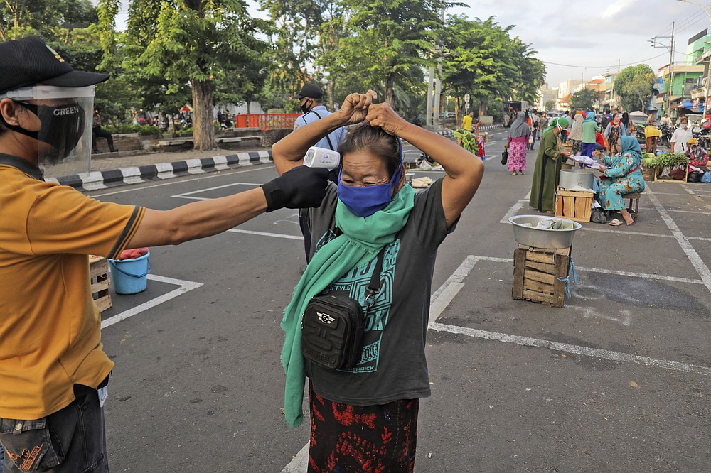 FILE - In this June 3, 2020, file photo, a city official takes the temperature reading of a vendor as others sit on a marked positions to maintain physical distancing in an attempt to curb the spread of the new coronavirus outbreak at a traditional market in Surabaya, East Java, Indonesia. As Indonesia’s overall virus caseload continues to rise, Jakarta's governor has moved to restore normalcy by lifting some restrictions, saying that the spread of the virus in the city of 11 million has slowed down after peaking in mid-April. This has raised concerns among some, with experts warning that reopening too soon can cause Jakarta to be hit with a second wave of the virus. (AP Photo/Trisnadi, File)