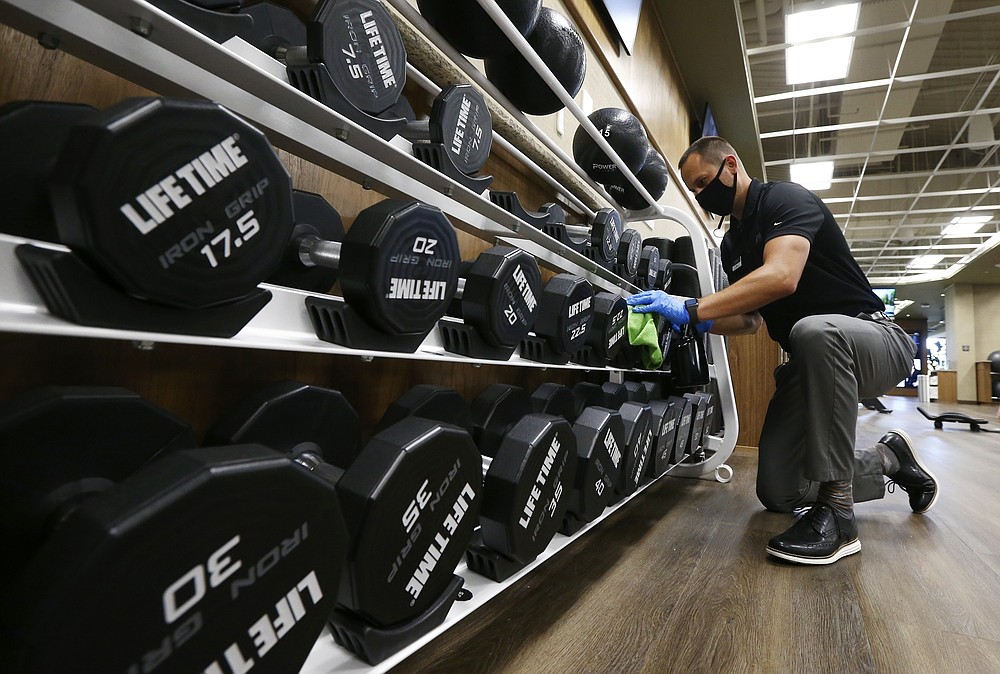 FILE - In this May 18, 2020, file photo, Jason Nichols, facilities operation manager at Life Time, disinfects hand weights at the Life Time Biltmore as it opens for business after being closed due to the coronavirus in Phoenix. Coronavirus cases are rising in nearly half the U.S. states, as states are rolling back lockdowns. (AP Photo/Ross D. Franklin, File)