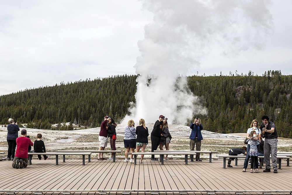 FILE - In this May 18, 2020 photo, visitors watch as Old Faithful erupts on the day the park partially reopened after a two-month shutdown due to the coronavirus pandemic, at Yellowstone National Park, Wyo. Lawmakers have reached bipartisan agreement on an election-year deal to double spending on a popular conservation program and devote nearly $2 billion a year to improve and maintain national parks. (Ryan Dorgan/Jackson Hole News & Guide via AP, File)
