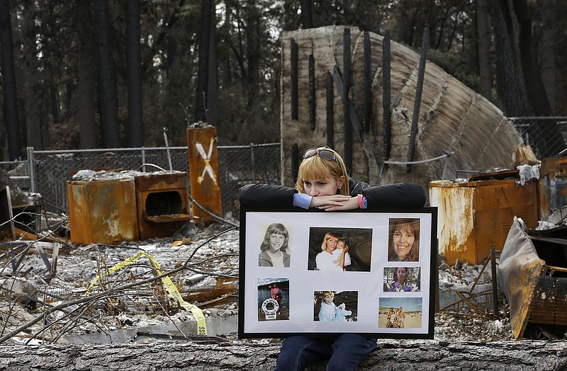 FILE - In this Feb. 7, 2019, file photo, Christina Taft, the daughter of Camp Fire victim Victoria Taft, displays a collage of photos of her mother, at the burned out ruins of the Paradise, Calif., home where she died in 2018. Pacific Gas & Electric officials are to be expected to appear in court Tuesday, June 16, 2020, to plead guilty for the deadly wildfire that nearly wiped out the Northern California town of Paradise in 2018. (AP Photo/Rich Pedroncelli, File)