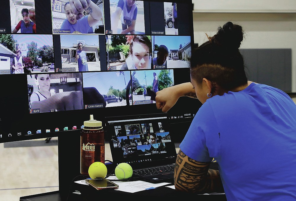 In this photo taken on Tuesday, June 9, 2020, VeAnne Navarro has a virtual fist bump with students including Bjarki Robertsson, lower left on screen, of Reykjavik, Iceland at Golden State Warriors basketball camp in Oakland, Calif. The Warriors had to adapt their popular youth basketball camps and make them virtual given the COVID-19 pandemic. (AP Photo/Ben Margot)