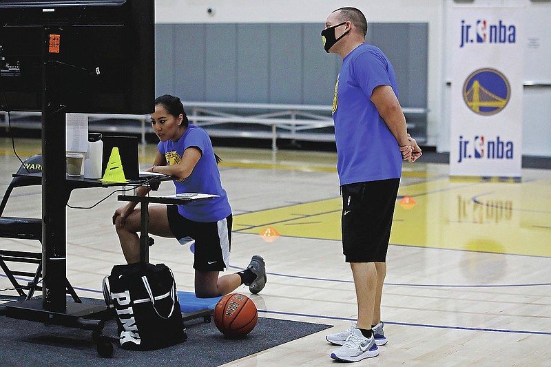 In this photo taken on Tuesday, June 9, 2020, Golden State Warriors basketball camp director Jeff Addiego, right, supervises coach Chanel Antonio as she speaks with her virtual students in Oakland, Calif. The Warriors had to adapt their popular youth basketball camps and make them virtual given the COVID-19 pandemic. (AP Photo/Ben Margot)