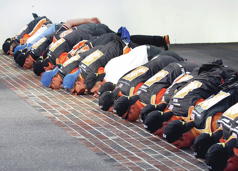 FILE - In this Sunday, July 29, 2007 file photo, NASCAR driver Tony Stewart and his crew kiss the bricks at the start/finish line after winning the Allstate 400 at the Brickyard auto race at the Indianapolis Motor Speedway in Indianapolis. On Friday, June 19, 2020, The Associated Press reported on stories circulating online incorrectly asserting that NASCAR, which recently banned the Confederate flag at its events, is now forcing its drivers to engage in Muslim prayer. Drivers at the Indianapolis Motor Speedway take part in a longstanding tradition called “kissing the bricks.” It was started by driver Dale Jarrett in 1996 after he won the Brickyard 400 race. (AP Photo/Doug McSchooler)