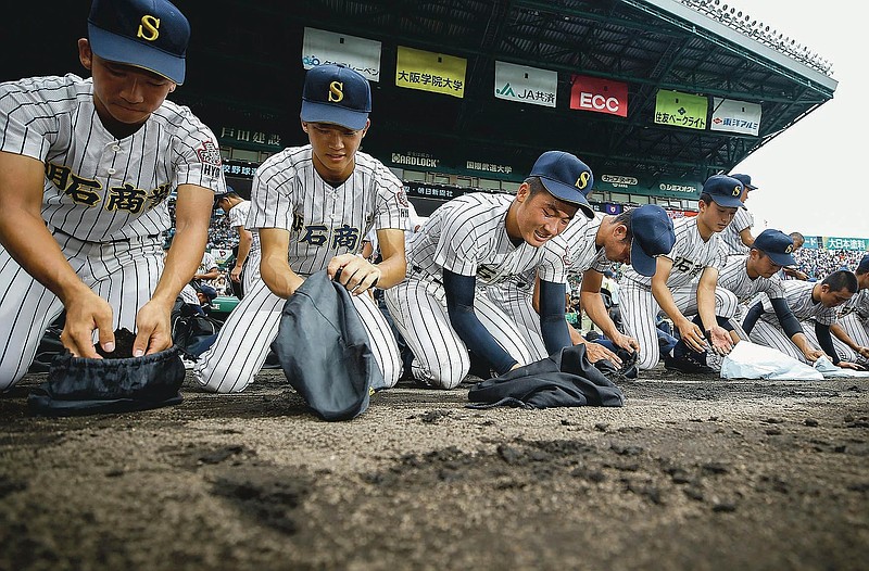 Akashi Commercial High School baseball players collect dirt of the grounds after being defeated by Riseisha High School during a semifinal game at the National High School Baseball Championship at Koshien Stadium in Nishinomiya, western Japan, on Aug. 20, 2019. Every year, after a team loses, the players, many weeping uncontrollably, scrape the dirt from foul territory near the dugout to take home as a memento. Japanese high school baseball players who had their heart set on going to the annual tournament won’t be able to go, with the 2020 event canceled over the coronavirus pandemic. (Kyodo News via AP)