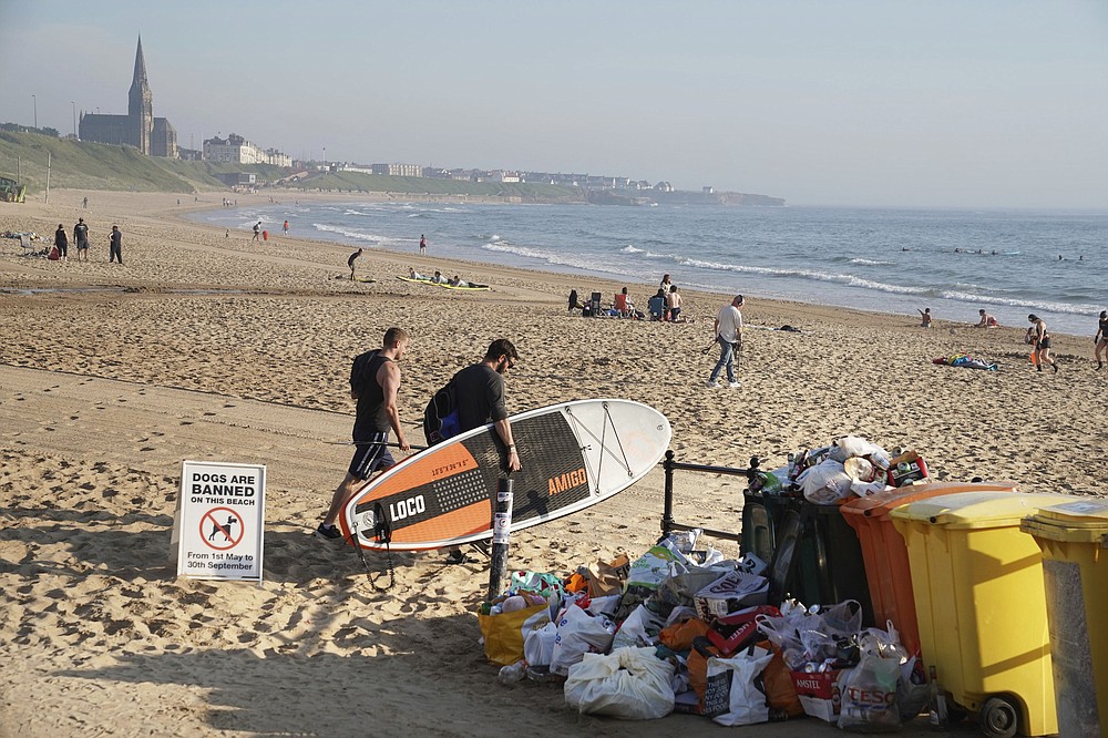 A man carrying a paddleboard passes rubbish collected by locals at Tynemouth beach after crowds gathered Thursday, in north east England, Friday June 26, 2020. British Health Secretary Matt Hancock has warned that the government has the power to close beaches and other public spaces in England amid growing concerns over the public's adherence to coronavirus social distancing rules. (Owen Humphreys/PA via AP)