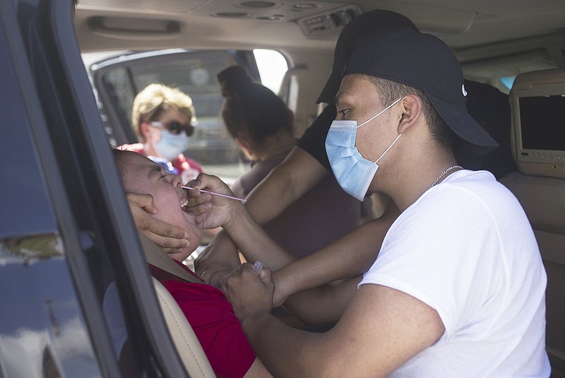 Johnathan Hinojosa of Rogers (right) administers a nasal swab to Justin Gonzalez, 4, (left), Friday, June 26, 2020 during a mass covid-19 screening at the Northwest Arkansas Community College in Bentonville. The Arkansas Department of Health hosted a mass screening for anyone at the campus. (NWA Democrat-Gazette/Charlie Kaijo)