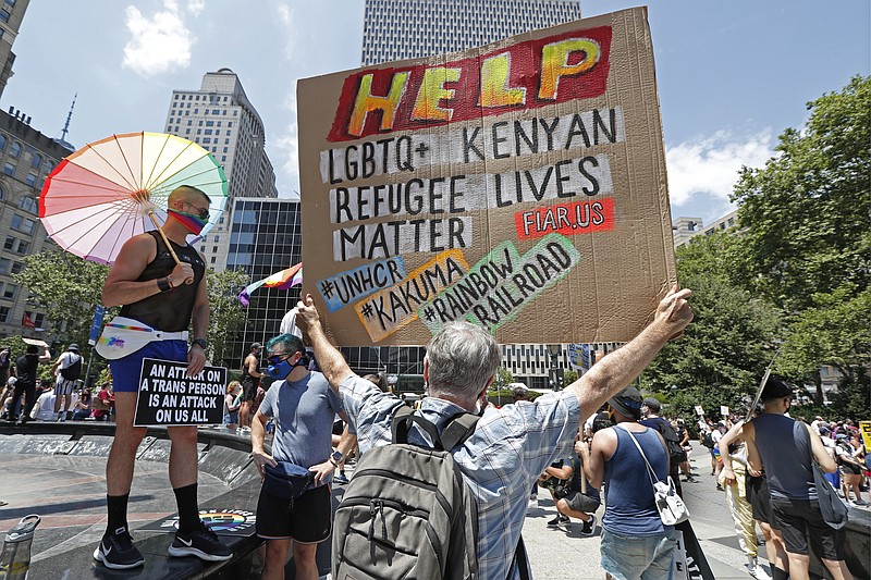 A person holds a sign as another person protects themself from the midday sun with a rainbow color umbrella as poeple gathered for the start of a queer liberation march for Black Lives Matter and against police brutality, Sunday, June 28, 2020, in New York. (AP Photo/Kathy Willens)