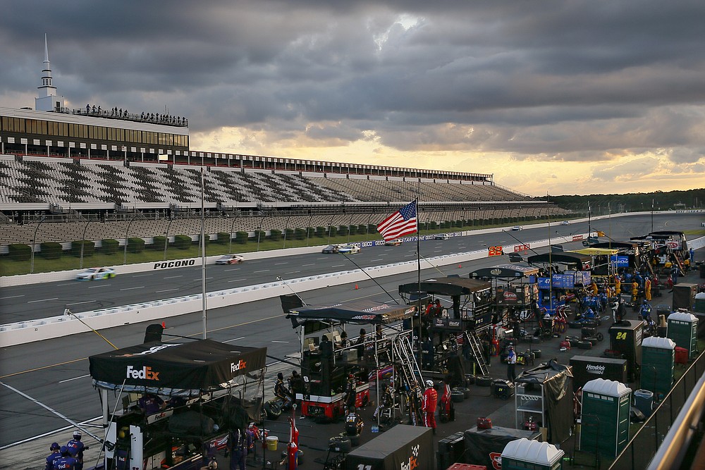 Racers speed down the front straight between the empty grandstand and their crews that are stationed along pit row as the sun goes down during a NASCAR Cup Series auto race at Pocono Raceway, Sunday, June 28, 2020, in Long Pond, Pa. (AP Photo/Matt Slocum)