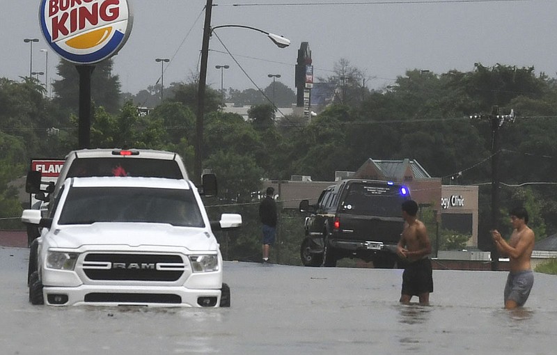 Two unidentified men wade through thigh-high waters to get to their vehicle in the 3500 block of Central Avenue on Monday. - Photo by Grace Brown of The Sentinel-Record