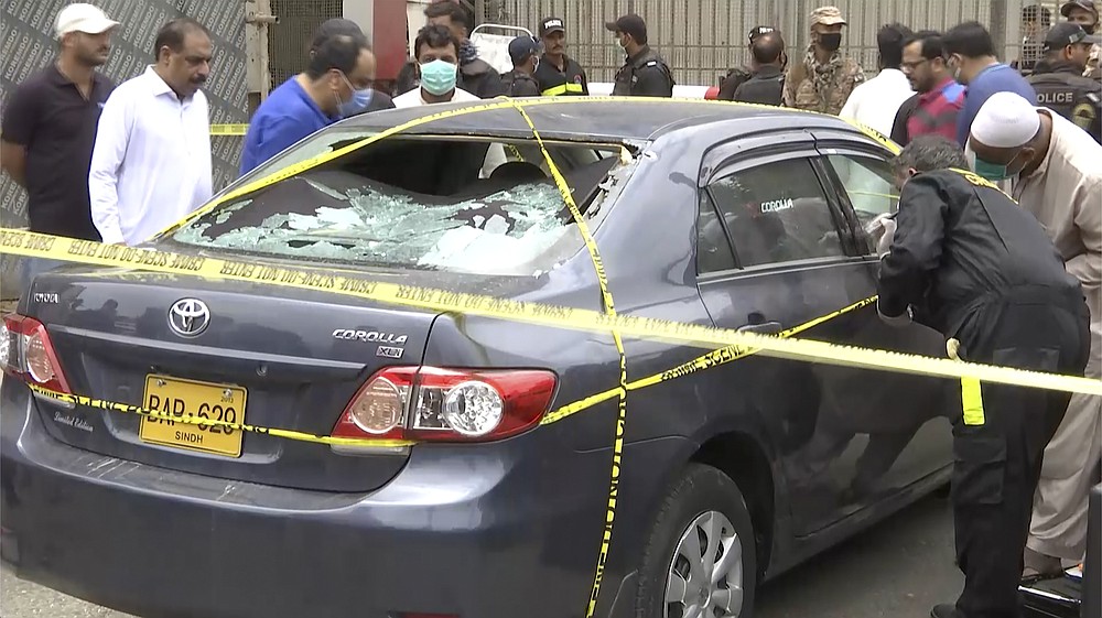In this image made from a video, police and investigators gather around a car used by attackers, in Karachi, Pakistan Monday, June 29, 2020. Militants attacked the stock exchange in the Pakistani city of Karachi on Monday, according to police. (AP Photo)
