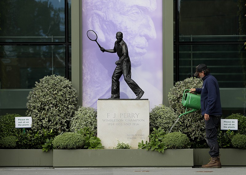 A gardener waters the plants alongside a statue of former Wimbledon Champion Fred Perry at the All England Lawn Tennis Club in Wimbledon in London Monday. The 2020 Wimbledon Tennis Championships, that were due to start today but have been cancelled due to the Coronavirus pandemic. - Photo by Kirsty Wigglesworth of The Associated Press story.lead_photo.caption