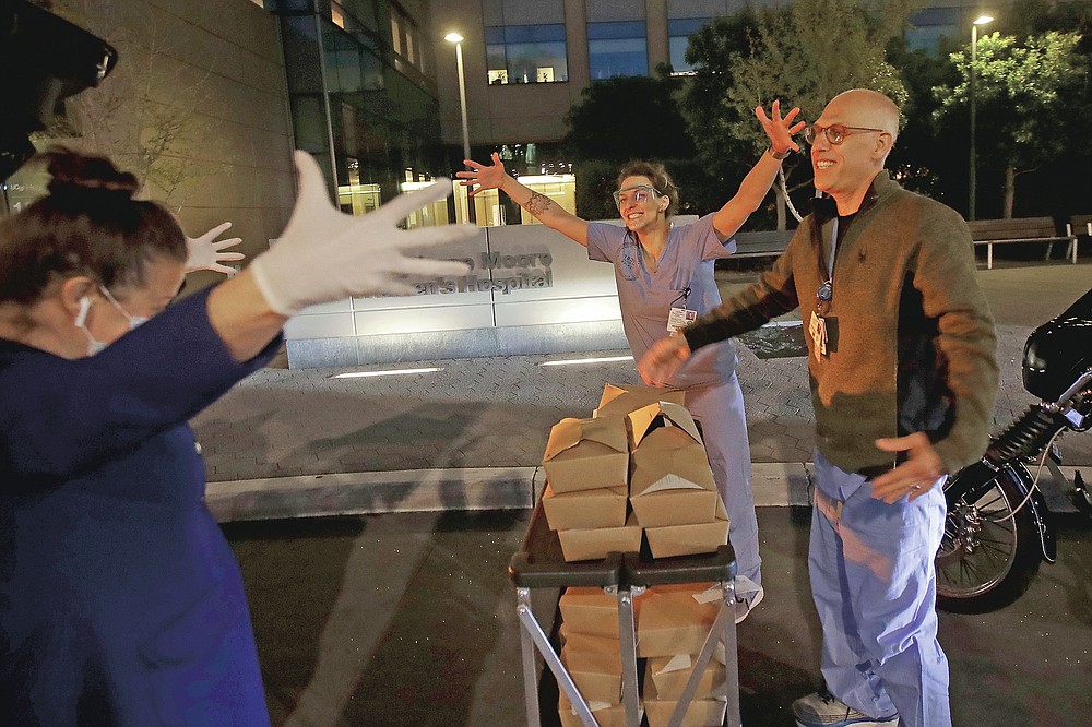 Nightbird Restaurant chef and owner Kim Alter, left, mimics giving a hug to nurse practitioner Sydney Gressel, center, and patient care technician Matt Phillips after delivering dinner to them at University of California at San Francisco Benioff Children's Hospital in San Francisco, March 27, 2020. A group of tech-savvy, entrepreneurial San Francisco friends wanted to help two groups devastated by the coronavirus pandemic. They came up with a plan that involved soliciting donations, tapping friends in the restaurant world and getting San Francisco hospitals to accept free food cooked up by some of the city's top chefs. (AP Photo/Jeff Chiu)