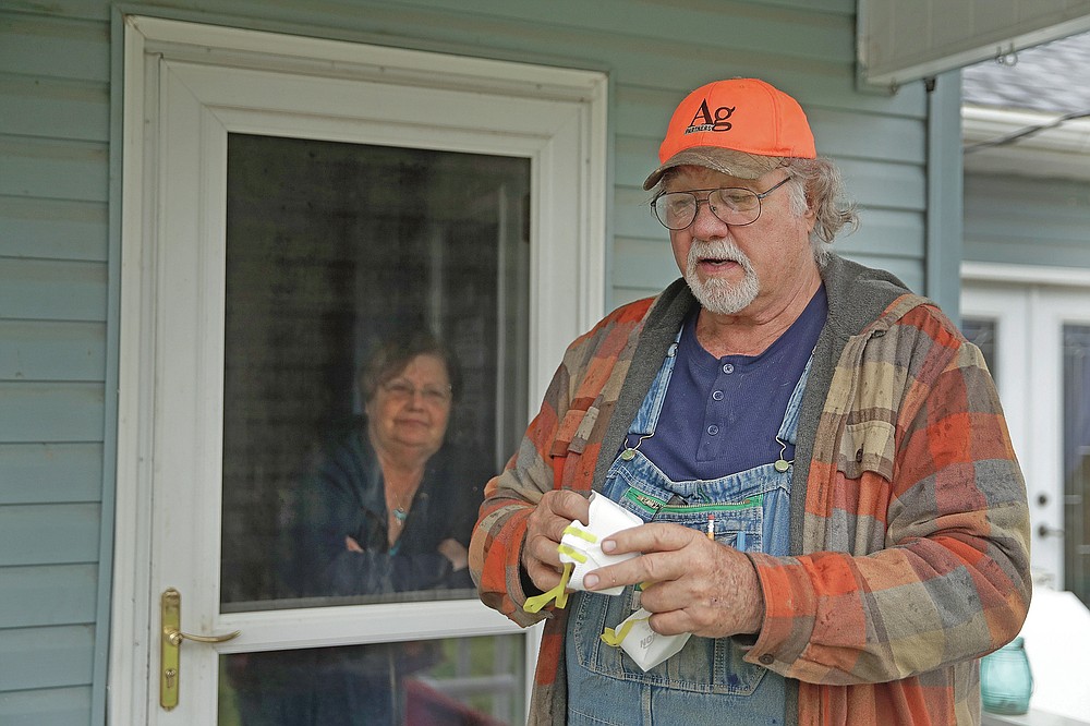 FILE - In this Friday, April 24, 2020 file photo, Dennis Ruhnke holds two of his remaining N-95 masks as he stands with his wife, Sharon at their home near Troy, Kan. Dennis, a retired farmer, shipped one of the couple's five masks left over from his farming days to New York Gov. Andrew Cuomo for use by a doctor or a nurse. (AP Photo/Charlie Riedel)