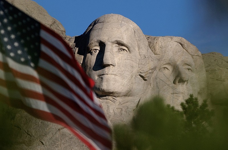 FILE - In this Sept. 11, 2002, file photo, the sun rises on Mt. Rushmore National Memorial near Keystone, S.D. as the flag is flown at half staff in honor of the first anniversary of the Sept. 11 terrorist attacks against the United States. When President Donald Trump speaks at the Mount Rushmore national memorial Friday, July 3, 2020, before the first fireworks show there in years, he'll stand before a crowd of thousands of people who won't be required to socially distance or wear masks despite the coronavirus pandemic. Public health experts say the lack of social distancing and enforced mask wearing could lead to a surge in the disease, while the fireworks risk setting the surrounding forest ablaze.(AP Photo/Laura Rauch, File)