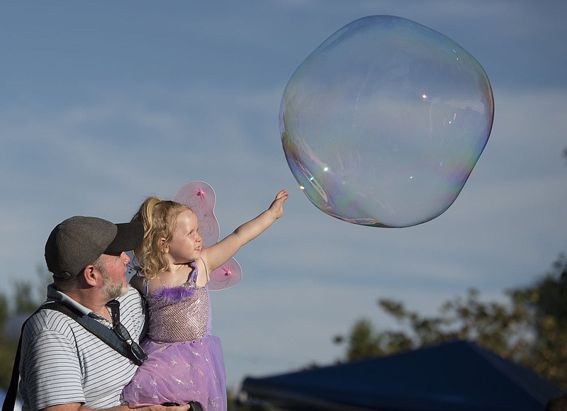 NWA Democrat-Gazette/J.T. WAMPLER Sean Dempsey of Fayetteville holds his daughter Ada, 2, while she stretches to touch a soap bubble during the annual Firefly Fling Saturday July 15, 2017 at the Botanical Garden of the Ozarks. The event also included garden fairies, food trucks, glowing games, fairy house building, fire dancing, nature stations and puppet performances.