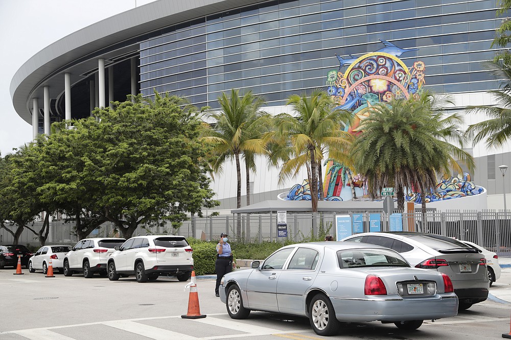 Vehicles pass by the home run sculpture as they wait in line outside of Marlins Park at a COVID-19 testing site during the coronavirus pandemic, Monday, July 6, 2020, in Miami. The long line of cars each morning as players arrive at work provides a reminder of the risks when they leave. Behavior away from the ballpark will be a big factor in determining whether Major League Baseball's attempt to salvage the 2020 season can succeed. (AP Photo/Lynne Sladky)