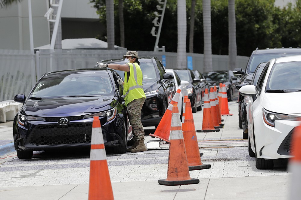 A member of the Florida National Guard monitors vehicles waiting in line outside of Marlins Park at a COVID-19 testing site during the coronavirus pandemic, Monday, July 6, 2020, in Miami. The long line of cars each morning as players arrive at work provides a reminder of the risks when they leave. Behavior away from the ballpark will be a big factor in determining whether Major League Baseball's attempt to salvage the 2020 season can succeed. (AP Photo/Lynne Sladky)