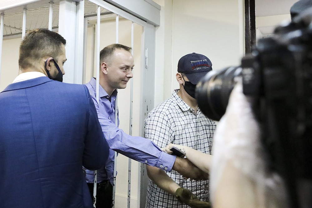 Ivan Safronov, an adviser to the director of Russia's state space corporation, second left, shakes hands with his supporters standing behind bars in a courtroom in Moscow, Russia, Tuesday, July 7, 2020. Safronov, a former journalist who worked as an adviser to the director of the Russian state space corporation, pleaded innocent to the treason charges against him. Ivan Safronov, a former journalist who served as an adviser to Roscosmos head Dmitry Rogozin, was detained in Moscow by agents of the Federal Security Service (FSB), the main KGB successor agency. (Sofia Sandurskaya, Moscow News Agency photo via AP)