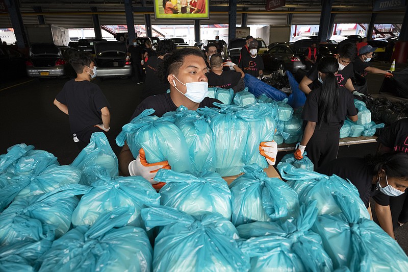 A worker moves bags of prepackaged meals to a sorting table where they will be loaded into insulated containers for delivery to needy families in New York, Tuesday, July 7, 2020. Catering startup HUNGRY originally served well-heeled office workers but with the downturn of the economy during the coronavirus pandemic it's now feeding the stuck-at-home elderly and low-income kids.(AP Photo/Mark Lennihan) story.lead_photo.caption