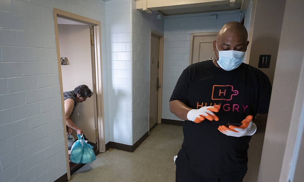Driver Frank Robinson confirms on his smart phone a delivery of food to a Brooklyn resident, left, Tuesday, July 7, 2020, in New York. The HUNGRY program "puts food on their table and it helps me to keep food on my table," says Robinson. (AP Photo/Mark Lennihan)
