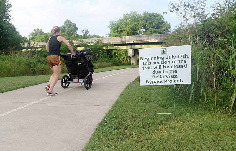 A jogger passes a sign on Wishing Springs Trail in Bentonville announcing the closure of the trail July 17th for construction of the Bella Vista Bypass. The city of Bentonville's facebook post says the section of trail which goes under I-49 and Walton Blvd. is expected to be reopened in the fall of 2021. (NWA Democrat-Gazette/Spencer Tirey)