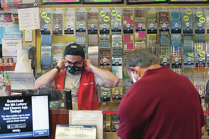 A clerk adjusts his protective mask while waiting on a masked customer at Ted's Stateline Mobil on Wednesday, June 24, 2020 in Methuen, Mass. The coronavirus pandemic has been a rollercoaster for state lotteries across the country, with some getting a boost from the economic downturn and others scrambling to make up for revenue shortfalls. (AP Photo/Charles Krupa)