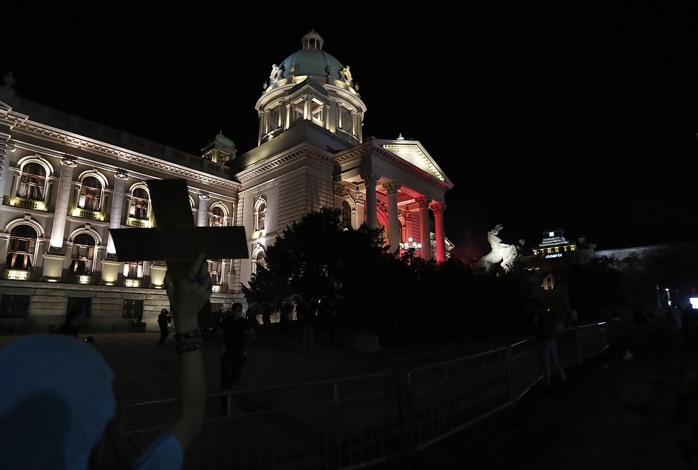 A woman holds a ceros and look at protesters clash with riot police on the steps of the Serbian parliament during a protest in Belgrade, Serbia, Friday, July 10 2020. Serbia's President Aleksandar Vucic said Friday he's not worried about losing political power amid large protests against his handling of the coronavirus crisis and hard-line rule, but instead expressed his fear about the spread of the virus by the demonstrators. The spontaneous protests started on Tuesday when Vucic announced that Belgrade would be placed under a new three-day lockdown following a second wave of confirmed coronavirus infections. (AP Photo/Darko Vojinovic)