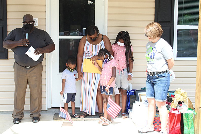 Garland County Habitat for Humanity dedicated its 146th home on Linwood Street on Saturday morning. Minister Bobbie Hampton of Roanoke Baptist Church, left, leads a prayer for the homeowner, his granddaughter, Ashley Hampton, center, who is surrounded by her children, from left, Malik, Sa’Brina and Ta’Kayla, and Habitat Executive Director Cindy Wagstaff, right. - Photo by Tanner Newton of The Sentinel-Record