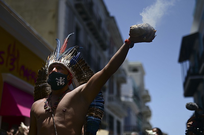 Gypsy Cordova spreads incense smoke while leading a group of activists in a march demanding statues and street names commemorating symbols of colonial oppression be removed, in San Juan, Puerto Rico, Saturday, July 11, 2020.  Dozens of activists marched through the historic part of Puerto Rico’s capital on Saturday to demand that the U.S. territory’s government start by removing statues, including those of explorer Christopher Columbus.  (AP Photo/Carlos Giusti)