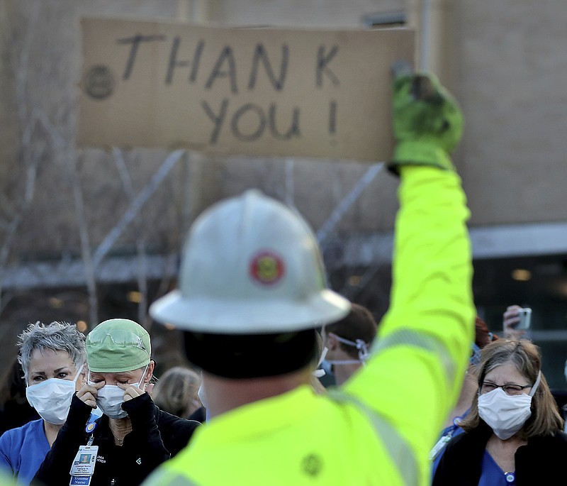 In this April 22 file photo healthcare workers, including ER nurse Tamra Hill, front left, wiping away tears, gather at Regions Hospital to thank Xcel Energy crew members, including Paul Peikert, who had lined the street outside Regions to greet healthcare workers at a morning shift change in St. Paul, Minn. Fewer than one-third of the states have enacted policies that shift the burden of proof for coverage of job-related COVID-19 so workers like first responders and nurses don't have to show they got sick by reporting for a risky assignment. - David Joles/Star Tribune via AP