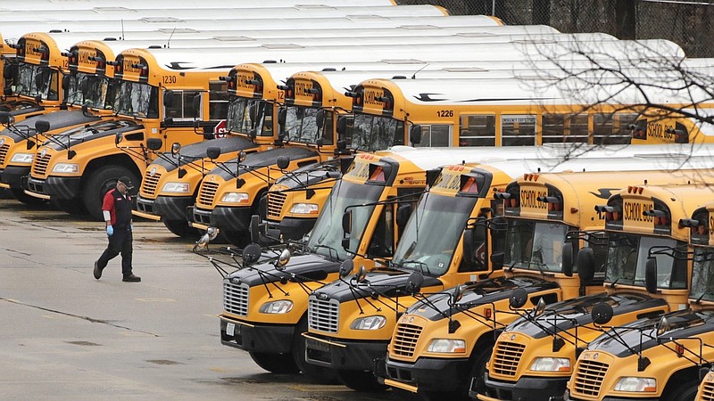 FILE - In this April 27, 2020, file photo, a worker passes public school buses parked at a depot in Manchester, N.H. As the Trump administration pushes full steam ahead to force schools to resume in-person education, public health experts warn that a one-size-fits-all reopening could drive infection and death rates even higher. (AP Photo/Charles Krupa, File)