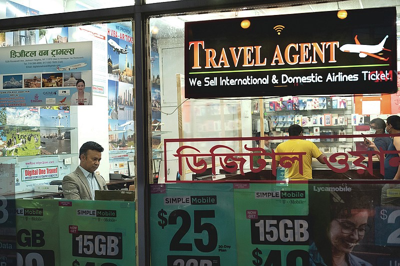 Zakaria Masud, left, works in his Queens travel agency after it reopened during the coronavirus pandemic, June 18, 2020, in New York's Jackson Heights neighborhood. "I think we're losing 50 percent of the revenue. But I think we can survive," said Masud. (AP Photo/Mark Lennihan)