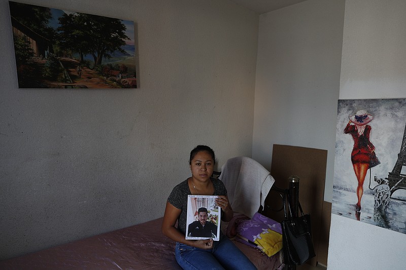 In this Feb. 13, 2020 photo, Alondra Mora holds a picture of her husband, Miguel Flores Lopez, 38, who disappeared Jan. 10, as she sits on the single bed the couple shared in the two-bedroom home where they lived with their four children, in Irapuato, Guanajuato state, Mexico. The Jalisco New Generation cartel is mounting a propaganda campaign in the area, using videos and social media to threaten rivals, while promising civilians that it won't prey on them with extortion and kidnappings. (AP Photo/Rebecca Blackwell)
