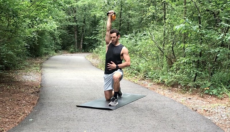 Eric Godwin demonstrates the Single Arm Half Kneeling Shoulder Press for Matt Parrott's Master Class on a trail near Little Rock Athletic Club. (Arkansas Democrat-Gazette/Celia Storey)