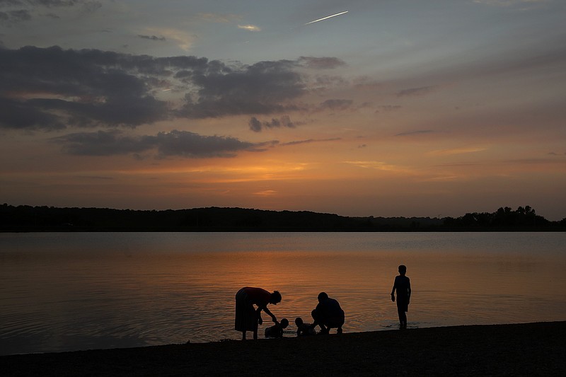 In this June 28, 2020 file photo, a family cools off in Shawnee Mission Lake at dusk in Lenexa, Kan. Many people have more time than money this summer, which offers a great opportunity to make some money moves that are free. (AP Photo/Charlie Riedel, File)