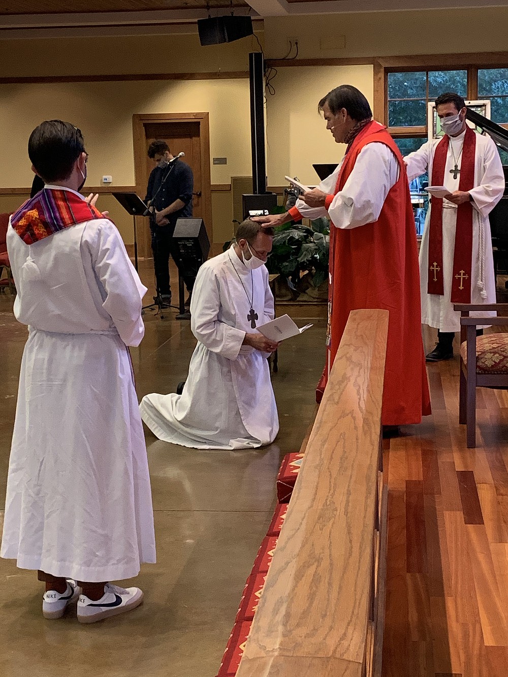 Dr. Nate Smith, kneeling, is consecrated as an Anglican priest by Bishop Phillip Jones as the Rev. Seth Richardson (left) and the Rev. Dustin Freeman (right) pray over him.
(Special to the Democrat-Gazette)