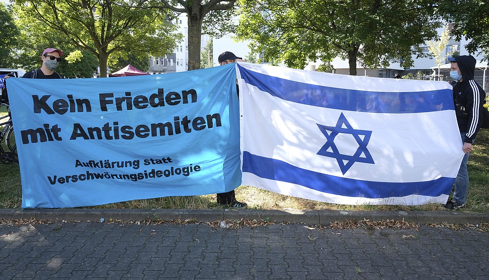 Participants of a rally stand with banners reading 'No peace with antisemites' in front of the regional court in Magdeburg, Germany, Tuesday, July 21, 2020. This is where the trial against the assassin of Halle begins. The Federal Prosecutor's Office accuses the man of 13 criminal offences, including murder and attempted murder. The assassin had tried to cause a bloodbath in the synagogue in Halle on October 9, 2019, the highest Jewish holiday Yom Kippur. (Sebastian Willnow/dpa via AP)