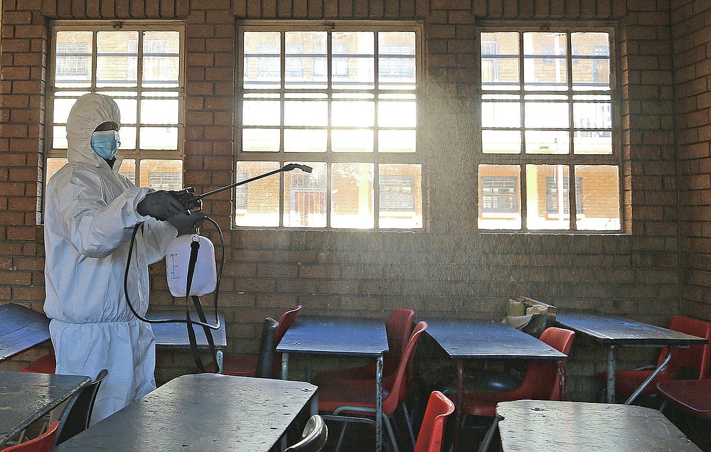 FILE - In this May 26, 2020, file photo, a worker from Bidvest Prestige wearing personal protective equipment, sprays disinfectant in a classroom to help reduce the spread the coronavirus ahead of the reopening of Landulwazi Comprehensive School, east of Johannesburg, South Africa. The options for African students eager to keep studying while schools remain closed because of the coronavirus pandemic seems varied, but the reality for many is that they will fall behind and possibly drop out of school forever, worsening inequality on an already unequal continent. (AP Photo/Themba Hadebe, File)