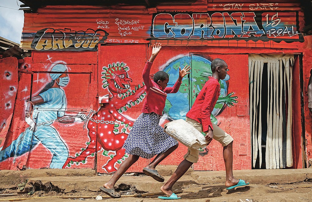 FILE - In this June 3, 2020, file photo, children run down a street past an informational mural warning people about the dangers of the new coronavirus, in the Kibera slum, or informal settlement, of Nairobi, Kenya. The options for African students eager to keep studying while schools remain closed because of the coronavirus pandemic seems varied, but the reality for many is that they will fall behind and possibly drop out of school forever, worsening inequality on an already unequal continent. (AP Photo/Brian Inganga, File)