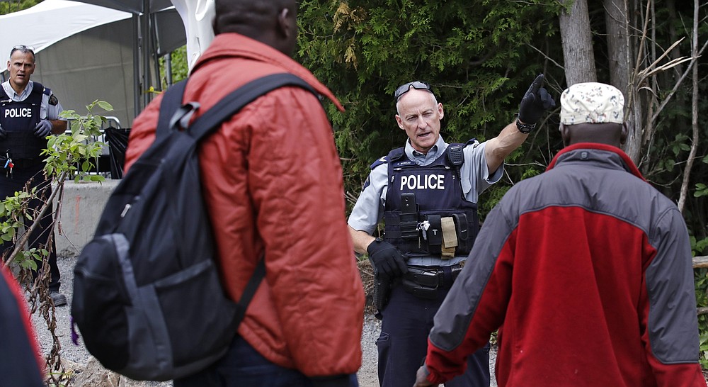 FILE - In this Aug. 7, 2017, file photo, Royal Canadian Mounted Police officers greet migrants as they enter into Canada at an unofficial border crossing at the end of Roxham Road in Champlain, N.Y. A Canadian court on Wednesday, July 22, 2020, invalidated the country's Safe Third Country Agreement with the United States. Under the agreement, immigrants who want to seek asylum in Canada at ground ports of entry from the United States are returned to the U.S. and told to seek asylum there. But if they request asylum on Canadian soil at a location other than an official crossing, the process is allowed to go forward. (AP Photo/Charles Krupa, File)