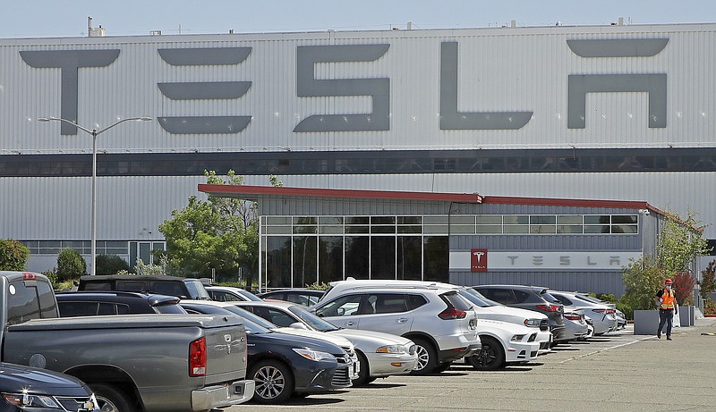 In this May 11 file photo, a man wearing a mask walks through the Tesla plant parking lot in Fremont, Calif. On Wednesday, the electric car maker announced it has picked the Austin, Texas, area as the site for its largest auto assembly plant employing at least 5,000 workers. - AP Photo/Ben Margot