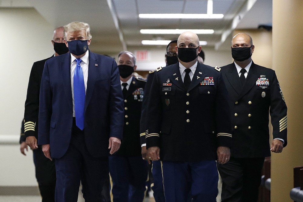 FILE - In this July 11, 2020, file photo President Donald Trump, foreground left, wears a face mask as he walks with others down a hallway during a visit to Walter Reed National Military Medical Center in Bethesda, Md. On Tuesday, July 21, Trump professed a newfound respect for the protective face masks he has seldom worn. “Whether you like the mask or not, they have an impact," he said. "I’m getting used to the mask,” he added, pulling one out after months of suggesting that mask-wearing was a political statement against him. (AP Photo/Patrick Semansky, File)