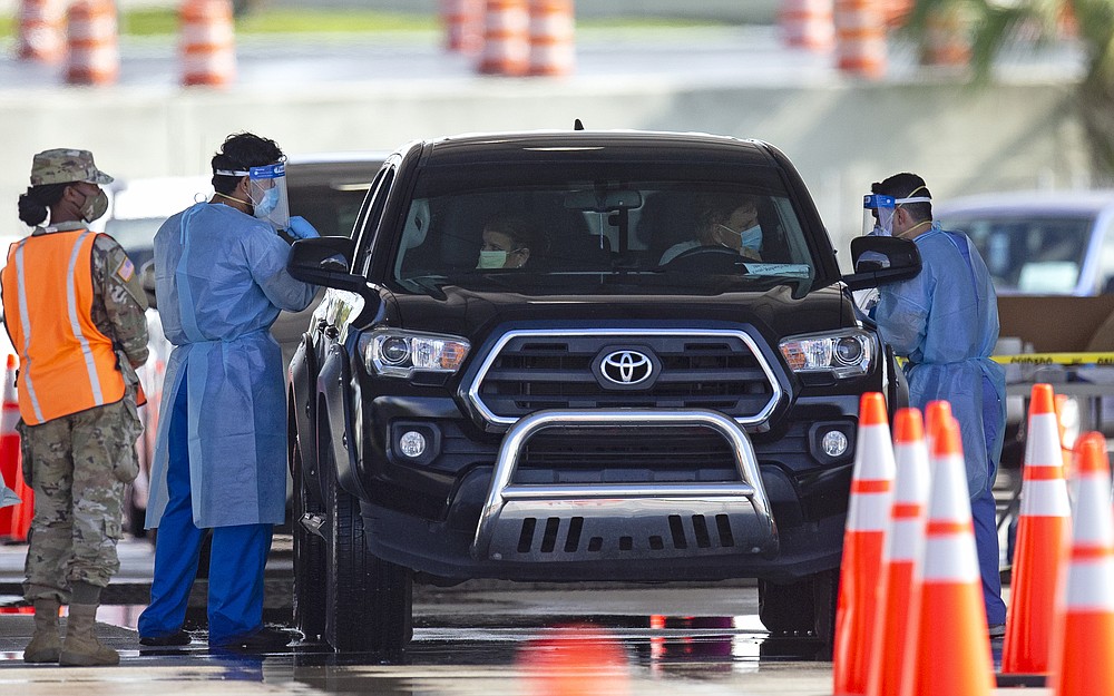A National Guard troop directs cars as a citizens are being tested by a healthcare workers at the COVID-19 drive-thru testing center at Hard Rock Stadium in Miami Gardens as the coronavirus pandemic continues on Sunday, July 19, 2020. (David Santiago/Miami Herald via AP)