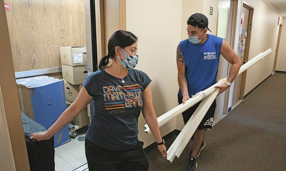 Joyce Lilly holds an elevator door as Xavier Jimenez moves belongings from her 14th floor apartment, Tuesday, July 21, 2020, in The Bronx borough of New York. If the coronavirus outbreak roars back in New York City, the Lilly family will not be sheltering again in their Bronx apartment. They just bought a house an hour north in the Hudson Valley. (AP Photo/Mark Lennihan)