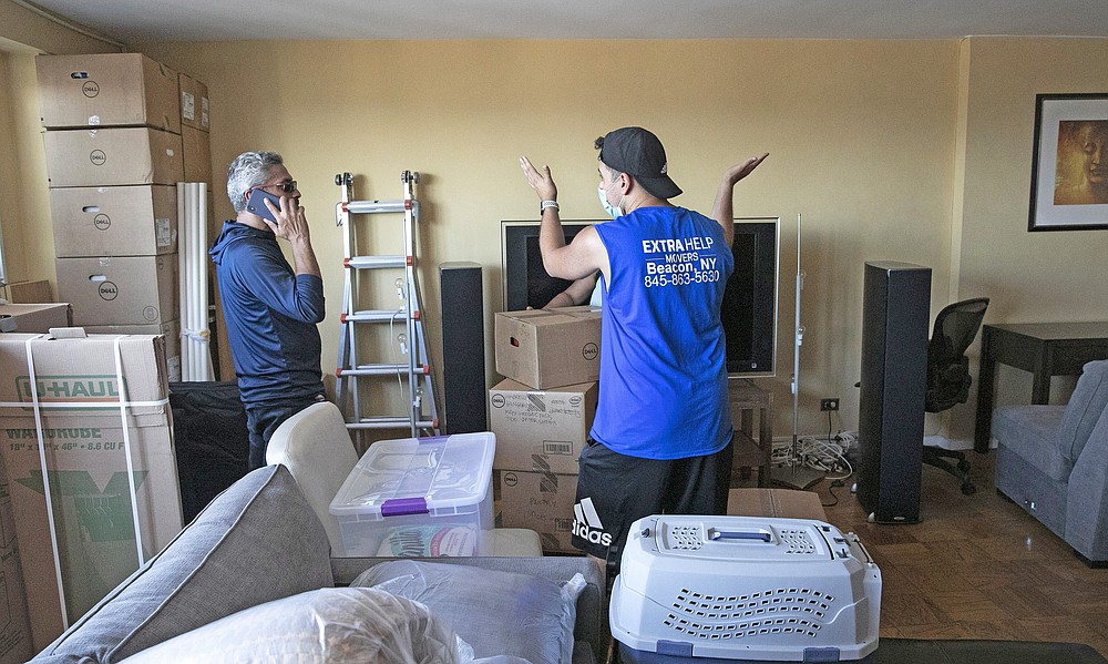 Anil Lilly, left, talks with his mover Xavier Jimenez as they stand in the Lilly's apartment, Tuesday, July 21, 2020, in The Bronx borough of New York. Anil and his wife, Joyce, are leaving the city for a home an hour's drive north, amid the coronavirus pandemic. He is an IT manager and his ability to work remotely was the deciding factor in the move. (AP Photo/Mark Lennihan)